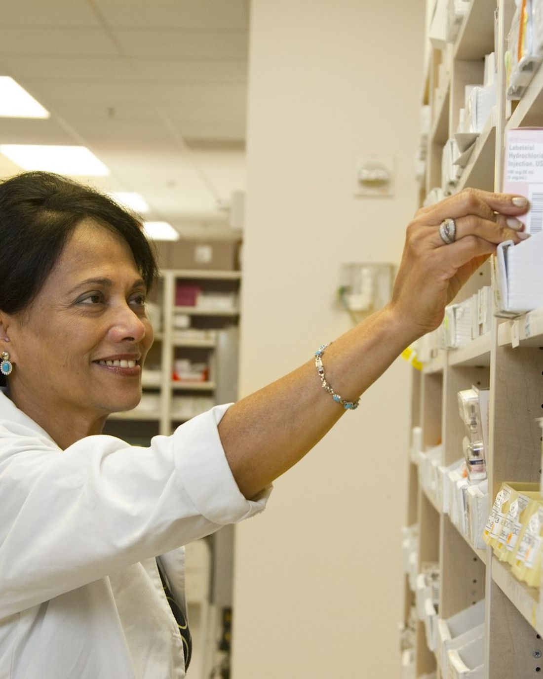 Auxiliar de farmacia organizando medicamentos en la estanteria de una drogueria.